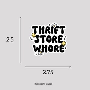 May include: Black and white sticker with the text "Thrift Store Whore" in a bold, rounded font. The sticker is decorated with small yellow smiley faces and white daisies.