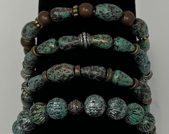 May include: Five turquoise and brown beaded bracelets with silver accents. The bracelets are stacked on a black surface.