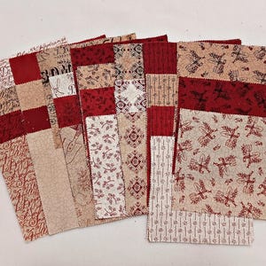May include: A collection of fabric squares in various patterns and colors. The squares feature a mix of red, beige, and white fabrics with designs including floral, script, and geometric patterns. Some squares have a patchwork design.