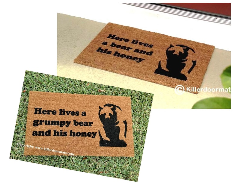 May include: A brown coir doormat with the text "Here lives a grumpy bear and his honey" and a black silhouette of a bear. The text "Copyright: www.killerdoormats.com" is at the bottom of the mat.