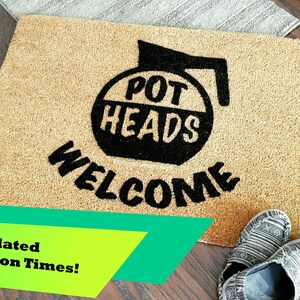 May include: A brown coir doormat with the text "POT HEADS WELCOME" in black lettering. The text is stylized to look like a coffee pot.