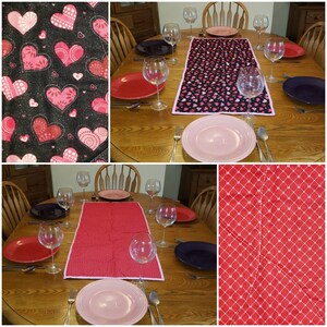May include: A wooden dining table set for a meal with red, pink, and purple plates, wine glasses, and silverware. Two table runners are visible, one with a black background and pink hearts, and another solid red with a white dotted pattern.