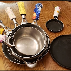 May include: A set of six different patterned pot holders, each with a different design. The pot holders are made of fabric and are designed to protect hands from hot cookware. The pot holders are shown on a wooden table with a variety of pots and pans.