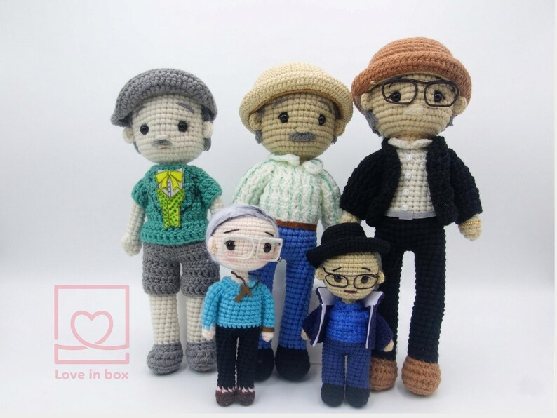 May include: Five handmade crochet dolls, each with unique outfits and accessories. The dolls feature hats, glasses, and various clothing items in shades of grey, blue, green, and brown. The dolls are standing on a white surface.
