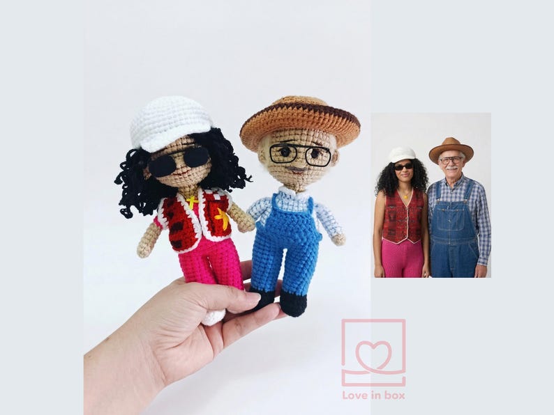 May include: Two crocheted dolls, one in a red vest and pink trousers, the other in blue dungarees. Both dolls wear hats and glasses. A smaller image shows the dolls' inspiration. The dolls are held in a hand.