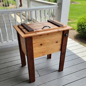 May include: A white ceramic mug with a black handle and the text "But First, Coffee" in a bold, black font. The mug is set against a blurred background, suggesting a cozy setting.