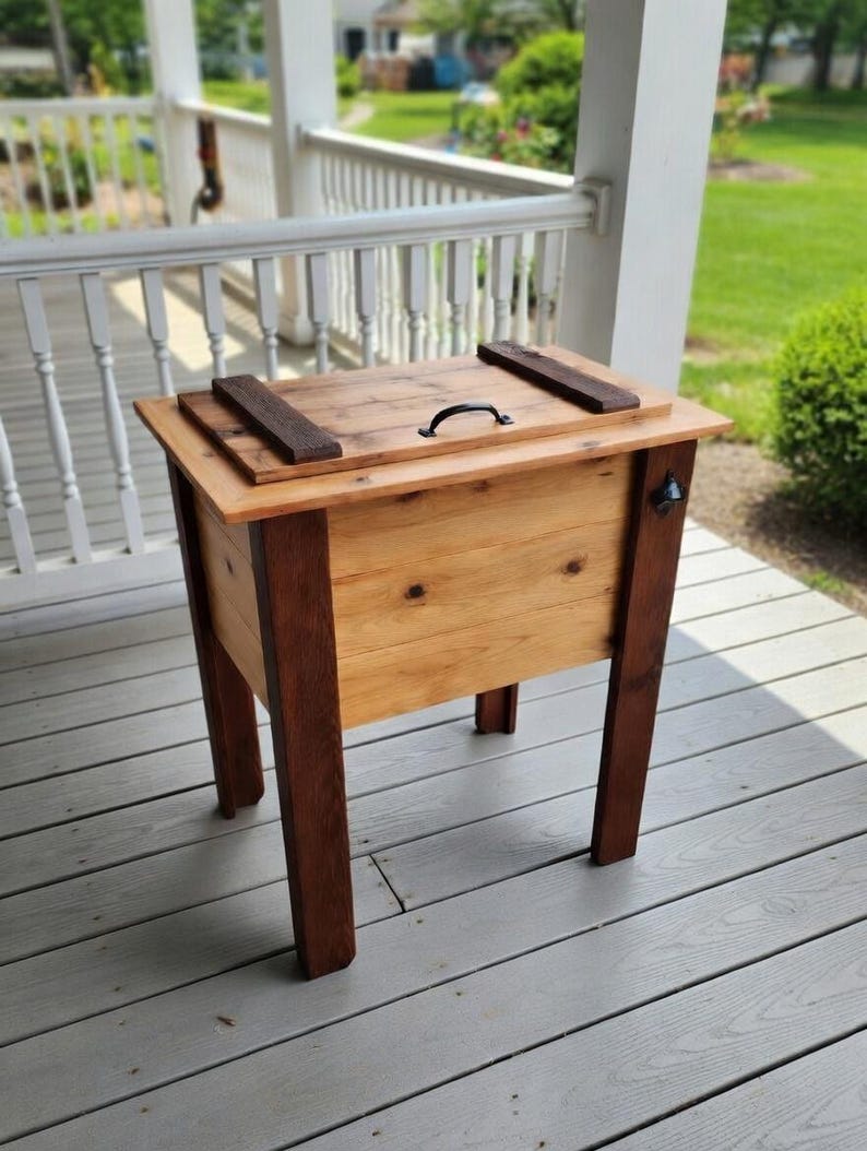 May include: A white ceramic mug with a black handle and the text "But First, Coffee" in a bold, black font. The mug is set against a blurred background, suggesting a cozy setting.