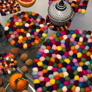 Puede incluir: Un juego de posavasos de fieltro de colores con una variedad de colores y patrones. Los posavasos están hechos de pequeñas bolas redondas de fieltro que están cosidas juntas. Los posavasos son perfectos para proteger tus muebles de platos y bebidas calientes.