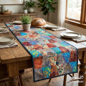 May include: A colorful patchwork table runner with a dark blue border. The runner features squares of various patterns and colors, including blue, orange, and floral designs. It is placed on a wooden table set for a meal.