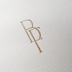 Puede incluir: Un monograma dorado con las letras "BF" entrelazadas.