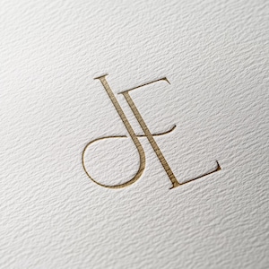 May include: A gold monogram featuring the letters "JE" intertwined.