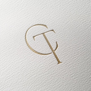 May include: A gold-colored monogram logo with the letters "CT" intertwined. The "C" is a circle and the "T" is a vertical line that extends through the circle.