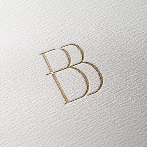 Op de afbeelding: Een goudkleurig logo met de letter "B" die drie keer wordt herhaald, waarbij elke "B" de andere overlapt.