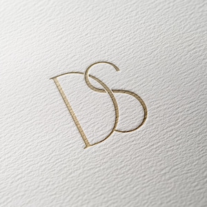 Könnte beinhalten: Ein goldenes Monogramm-Logo mit den ineinander verschlungenen Buchstaben "DS".