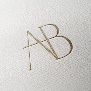 May include: A gold monogram logo with the letters "AB" intertwined.