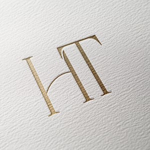 Peut inclure: Un monogramme de couleur or avec les lettres "HT" dans une police de caractères stylisée.