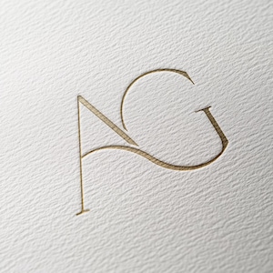 May include: A gold-coloured monogram logo with the letters "AG" intertwined.