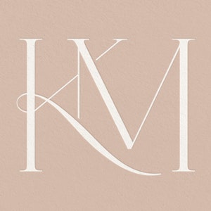 May include: White monogram with the letters "K" and "M" intertwined. The letters are in a script font and are set against a light pink background.