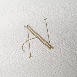 Op de afbeelding: Een gouden monogram van de letter "N" met een gestileerd ontwerp.