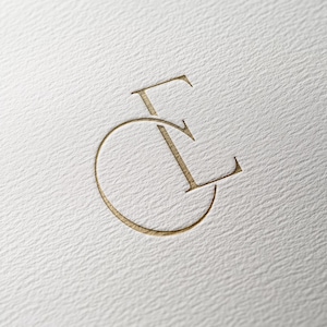 May include: A gold-colored monogram logo with the letters "C" and "E" intertwined.