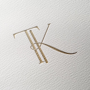 以下が含まれることがあります： 「TK」という文字が絡み合った金色のモノグラム。「T」は二重線で、「K」は筆記体です。