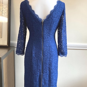 May include: A cobalt blue lace dress with long sleeves and a scalloped neckline. The dress features a full-length zipper down the back and is displayed on a mannequin. The dress is a knee-length style.
