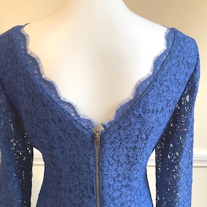 May include: A royal blue lace dress with long sleeves and a scalloped neckline. The dress features a brass zipper down the back. The intricate lace pattern and elegant design make it suitable for special occasions.