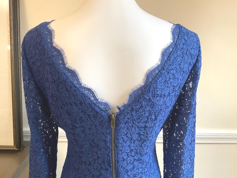 May include: A royal blue lace dress with long sleeves and a scalloped neckline. The dress features a brass zipper down the back. The intricate lace pattern and elegant design make it suitable for special occasions.