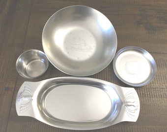 Puede incluir: Un juego de cuatro piezas de servicio de metal plateado que incluye un cuenco redondo grande con un velero grabado, un cuenco redondo pequeño, un plato redondo pequeño con diseño circular y una bandeja ovalada con asas en relieve.