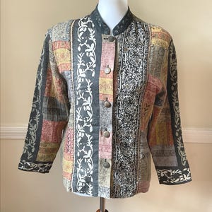 May include: A long-sleeve jacket featuring a patchwork design with various floral and geometric patterns in shades of gray, yellow, and muted red. The jacket has a mandarin collar, a front button closure with five metallic buttons, and long sleeves.