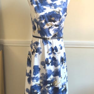 May include: A white sleeveless dress with a blue and gold abstract floral print. The dress has a black belt with a silver buckle.