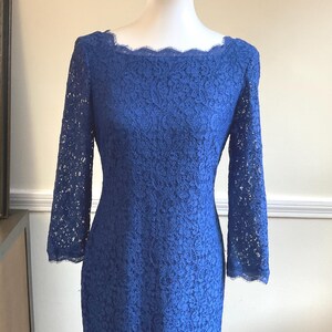 May include: A royal blue lace dress with long sleeves and a scalloped neckline. The dress is displayed on a mannequin, showcasing its intricate floral lace pattern. The sleeves extend to the mid-forearm.