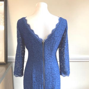 May include: A long-sleeved, navy blue lace dress with a scalloped neckline and a full-length zipper down the back. The dress is displayed on a mannequin, showcasing its intricate floral lace pattern.