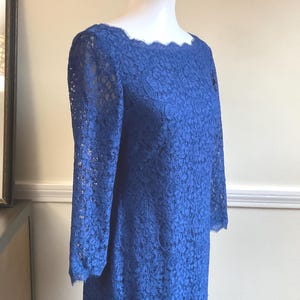 May include: A royal blue lace dress with long sleeves and a scalloped neckline. The dress is displayed on a mannequin, showcasing its intricate floral lace pattern. The dress is a classic style, suitable for formal occasions.