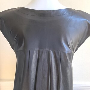 May include: A dark grey leather dress with a boat neck and cap sleeves. The dress has a pleated design below the bust and a subtle sheen. The dress is displayed on a mannequin.