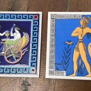 May include: Two square ceramic wall tiles featuring classical art. The left tile shows a figure in a purple robe offering a vessel to a seated figure in a winged chariot on a dark blue background. The right tile depicts a figure in a blue field with the text KNOSSOS.