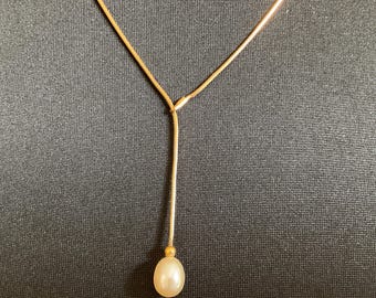 May include: A gold-toned Y-shaped necklace featuring a thin, flexible snake chain that meets at a central connector. A single, smooth, off-white teardrop-shaped pearl hangs from the bottom of the chain, accented by a small gold-toned bead.