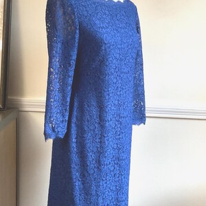 May include: A cobalt blue lace dress with long sleeves and a scalloped neckline. The knee-length dress is displayed on a mannequin. The dress has a floral lace pattern and a scalloped hemline. The dress is a vintage style.