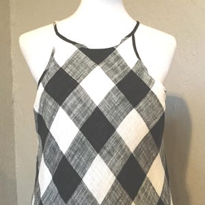 May include: A black and white checkered halter top dress displayed on a mannequin. The dress features a bold, oversized gingham pattern. The neckline and straps are outlined with a thin black trim. The fabric appears to be lightweight.