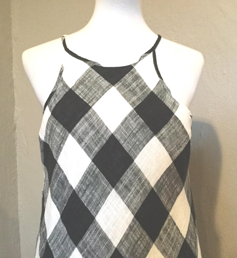 May include: A black and white checkered halter top dress displayed on a mannequin. The dress features a bold, oversized gingham pattern. The neckline and straps are outlined with a thin black trim. The fabric appears to be lightweight.