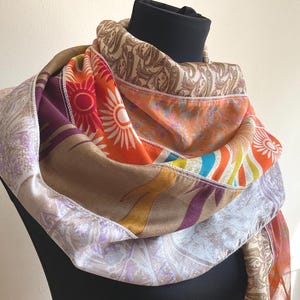 May include: A multi-colored scarf featuring a patchwork design of various fabrics. The scarf displays sections of orange with sunburst patterns, brown paisley prints, and light purple floral motifs, all joined together with visible white stitching.