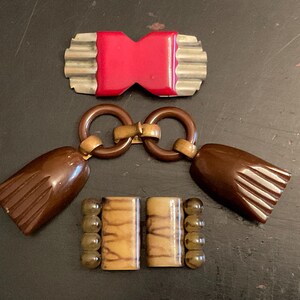 May include: Three vintage plastic and metal belt buckles. One is red and has a wavy metal frame. Another is brown with a tassel and a gold metal connector. The last is brown with a striped pattern and gold beads.