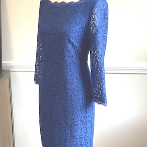 May include: A navy blue lace dress with a scalloped neckline and three-quarter sleeves. The dress is displayed on a mannequin. The dress is knee-length and has a fitted silhouette.