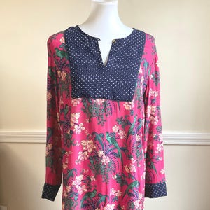 May include: A long-sleeved dress with a vibrant pink floral pattern featuring green birds and white flowers. The neckline and cuffs are navy blue with white polka dots. The neckline has a small gold-colored button.