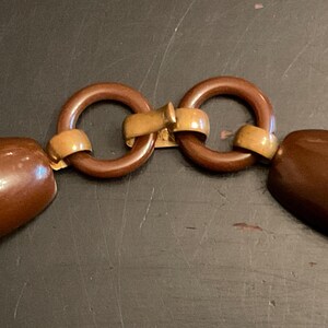 May include: A brown plastic clasp with two round rings and a gold metal connector. The clasp has a textured design on the ends.
