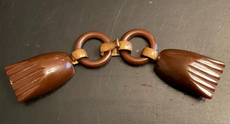 May include: A brown plastic clasp with two round rings and a gold metal connector. The clasp has a textured design on the ends.