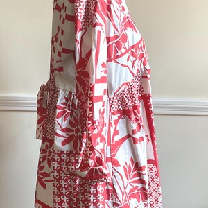May include: A long-sleeved shirt dress featuring a white base with a bold red graphic pattern of geometric shapes, floral motifs, and cross-hatch designs. The garment includes a classic collar, a button-down front, and a tie-waist detail at the back.