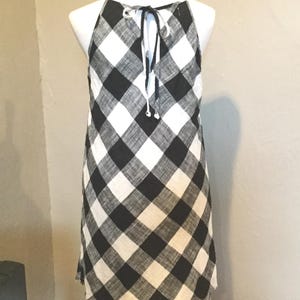 May include: A black and white checkered halter dress with a frayed hem. The dress is displayed on a mannequin. The dress has a tie closure at the back of the neck.