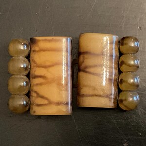 May include: A pair of brown and beige rectangular buttons with a wood grain pattern. The buttons are attached to a string of clear, round beads.