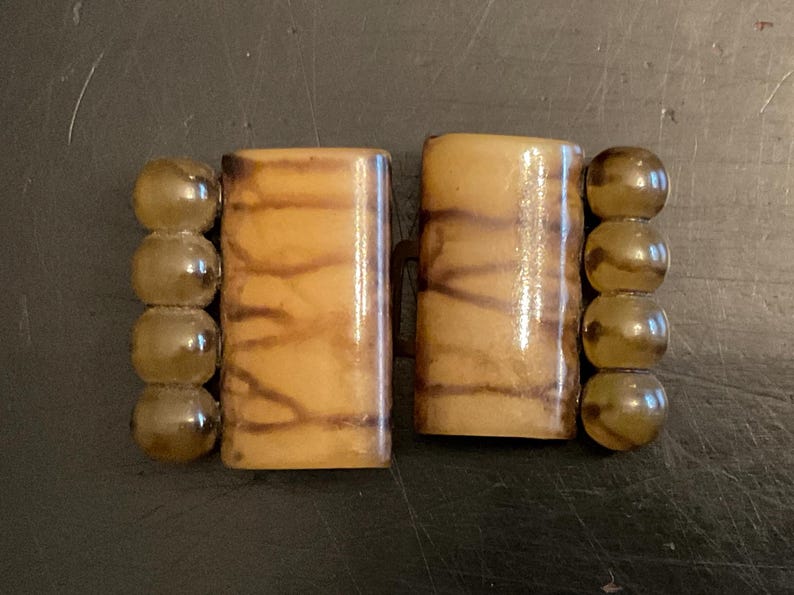 May include: A pair of brown and beige rectangular buttons with a wood grain pattern. The buttons are attached to a string of clear, round beads.